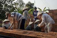 Workers load finished bricks onto waiting trucks